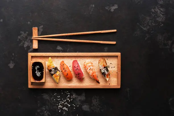 Photo of Close up of sashimi sushi set with chopsticks and soy sauce, dark stone background. Top view, copy space.