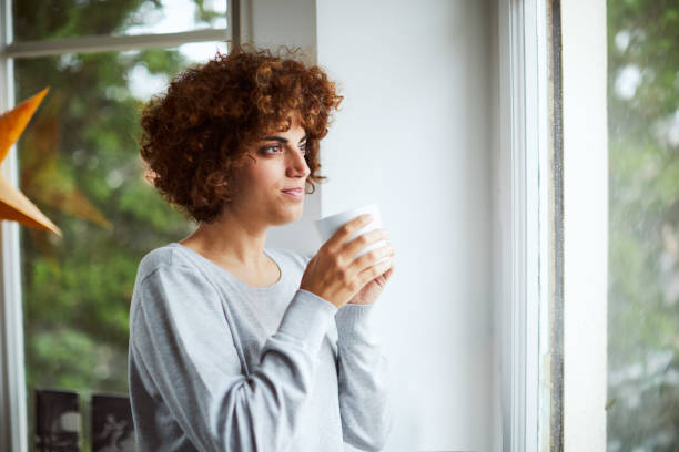 istock One woman looking thorough window and enjoying a cup of tea. 1131816595