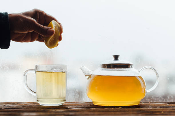 Senior adult hand squeezing a lemon with green tea pot stock photo