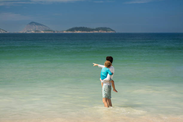 Father holds his son on the lap and points to the wave coming. Ipanema, Rio de Janeiro, Brazil.