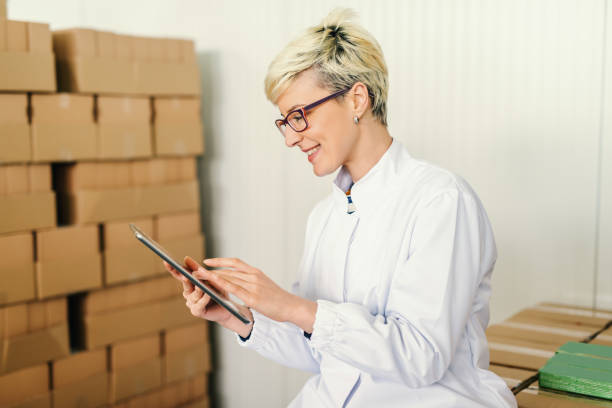 istock Happy Caucasian blonde employee suing tablet for work while sitting around boxes in food factory. 1131824948