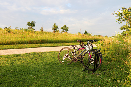 Scenic view with wild grasses field, rural road and pair of parked bicycles in a foreground during sunset. Summer nature background, healthy lifestyle concept.