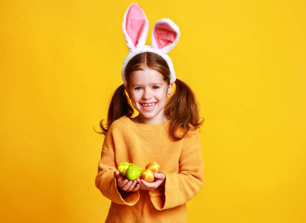 黄色のイースターエッグとバニー耳を持つおかしい幸せな子供の女の子 - easter egg easter yellow paint ストックフォトと画像