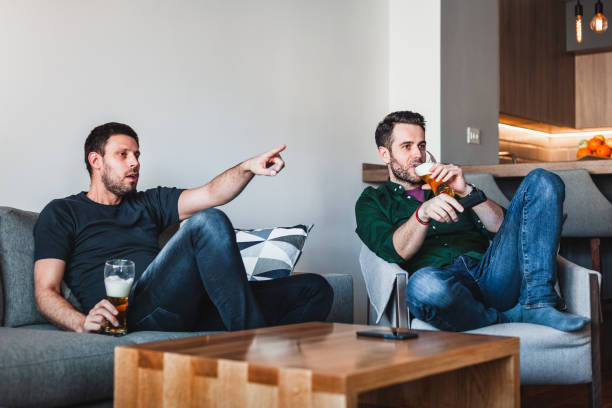istock Two guys drinking beer watching sports on TV 1131829854