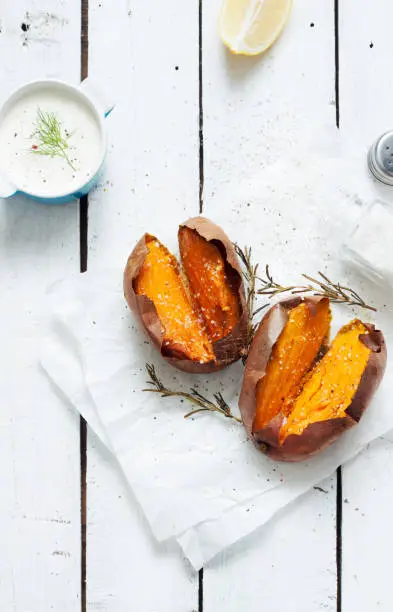 Photo of Baked sweet potatoes, dip, salt and rosemary on white wood from above