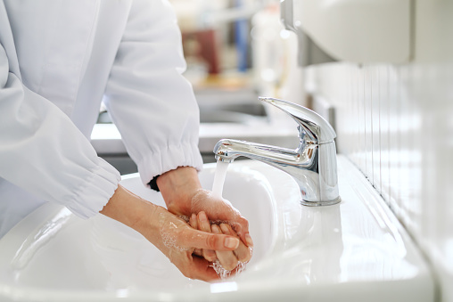 Close up of female employee washing hands in sink before working in food factory.