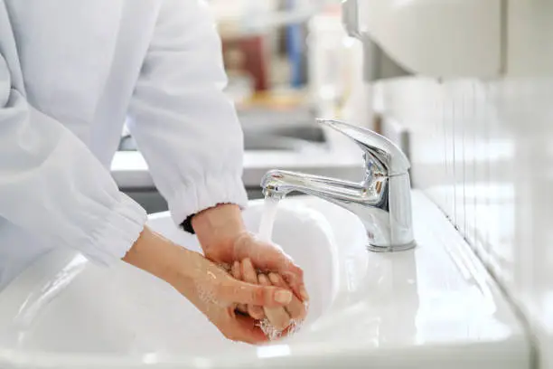 Photo of Close up of female employee washing hands in sink before working in food factory.