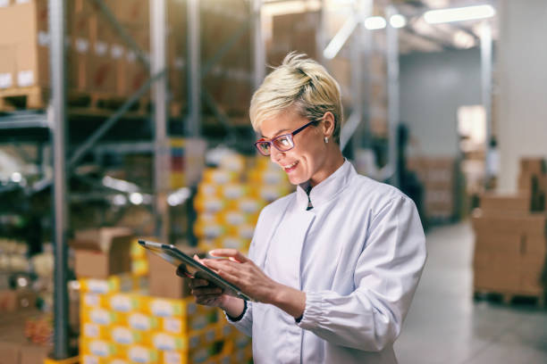 giovane donna bionda caucasica in uniforme bianca usando tablet in magazzino. - warehouse freight transportation checklist industry foto e immagini stock
