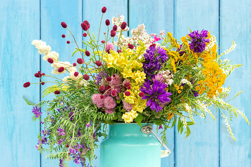 Bright colorful bouquet of wild flowers in starm tin can vase on background blue wooden boards. Template for postcard or your design Concept Women's day or Mothers Day, Hello summer Hello spring.