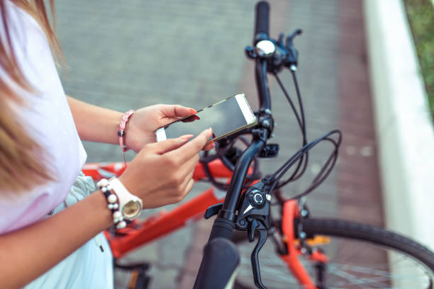 istock Girl is holding smartphone, searching route through application in Internet map. Against the background of red black bicycle in parking lot. Online in social networks, communication correspondence. 1131846986