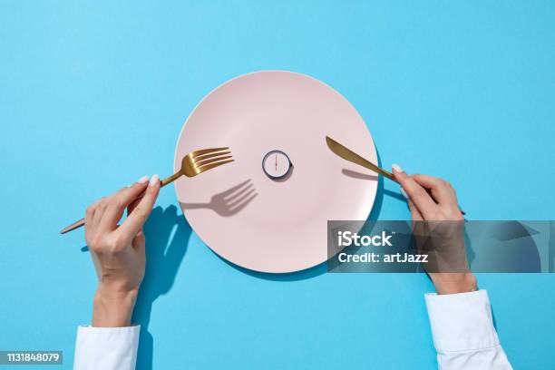 White Plate With Round Whatch Shows Six Oclock Served Knife And Fork In A Girls Hands On A Blue Background Time To Eat And Diet Concept Top View Stock Photo - Download Image Now