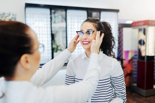 istock Optician putting on eyeglasses on patient and helping her to choose right frame. Optician store interior. 1131848593