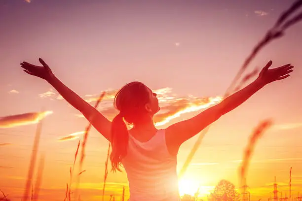 Photo of Free and happy woman raises arms against the sunset sky. Harmony and balance