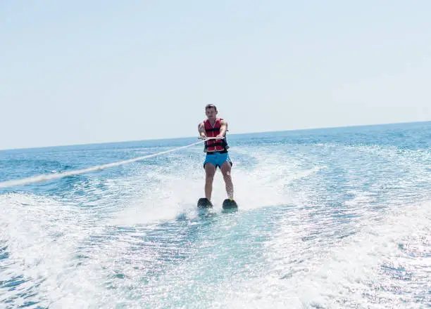 Photo of Young man glides on water skiing on the waves on the sea, ocean. Healthy lifestyle. Positive human emotions, joy. Family are spending time at tropical ocean in the day time. Miami beach.