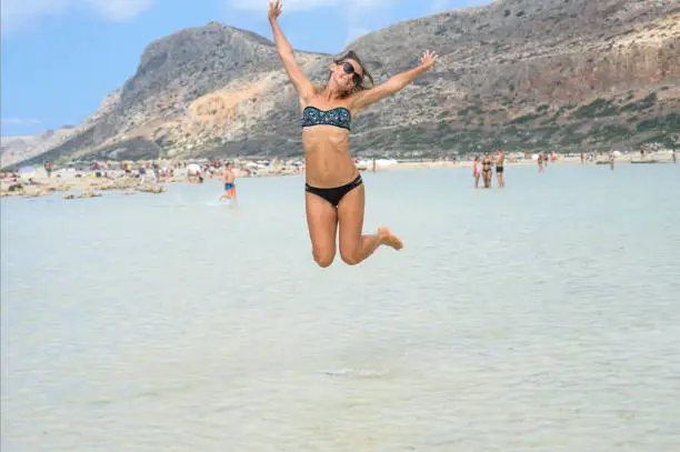 Photo of Happy smiling young woman is jumping on the beach. Concept of friendly family. Happy summer days. Balos Lagoon. Elafonisi Beach - Crete, Greece. - Image