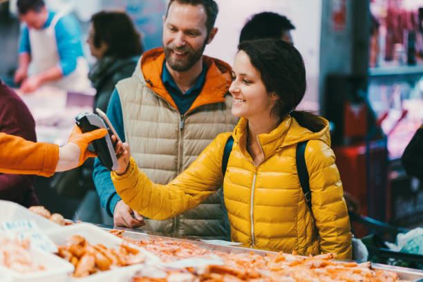 Couple in Valencia shopping at the fish market Young couple buying shrimps and paying contactless with mobile phone fish market photos stock pictures, royalty-free photos & images