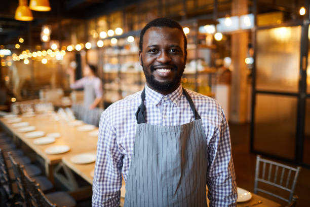 istock Excited confident handsome young black restaurant waiter with beard standing in modern restaurant and looking at camera 1131854967