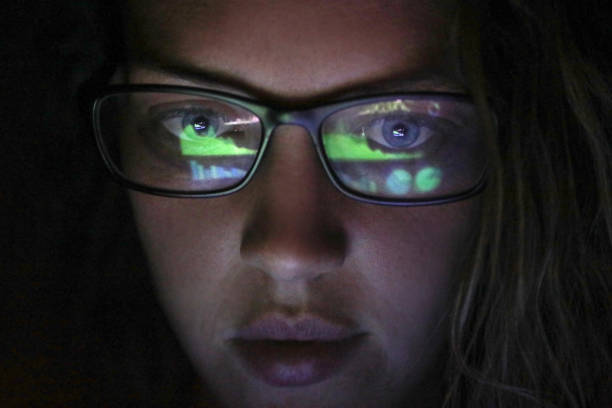 an Adult female looking at financial graphs on a laptop. an Adult female looking at financial graphs on a laptop in a dark room with financial graphs reflected in his glasses. computer hacker spy computer crime laptop stock pictures, royalty-free photos & images