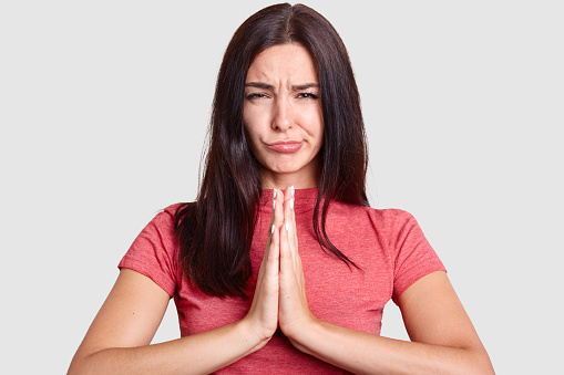 Brown haired lady wrinkle beautiful forehead in order to show emotions. These amazing hands with manicure are joined together and try to ask for forgiveness from love, because she is guilty.