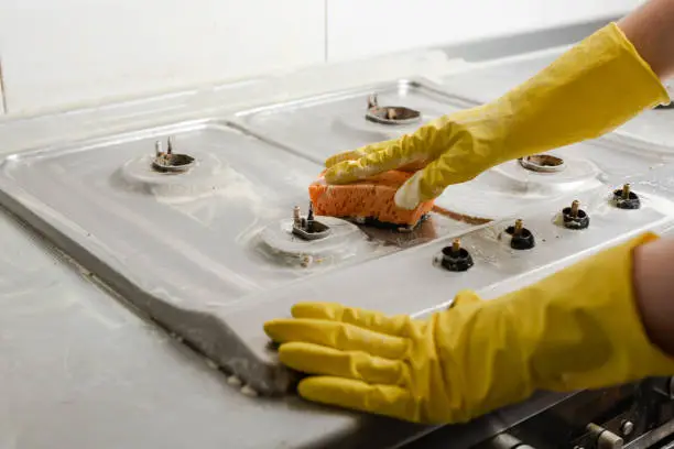 Photo of Hands in yellow gloves washing gas stove.