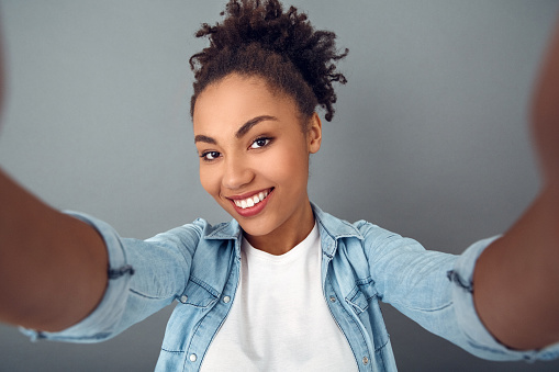 Young african female student isolated on grey wall taking selfie photos on camera close-up smiling happy