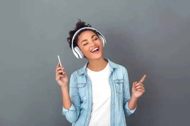 Photo of Young african woman isolated on grey wall studio casual daily lifestyle listening music