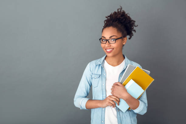 joven mujer africana aislado en gris pared estudio casual diario estilo de vida estudiante sosteniendo cuadernos sonriendo - college girl fotografías e imágenes de stock