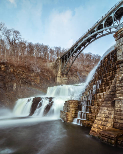 istock Water cascading down a dam with a bridge arching over the waterfall. 1131863545