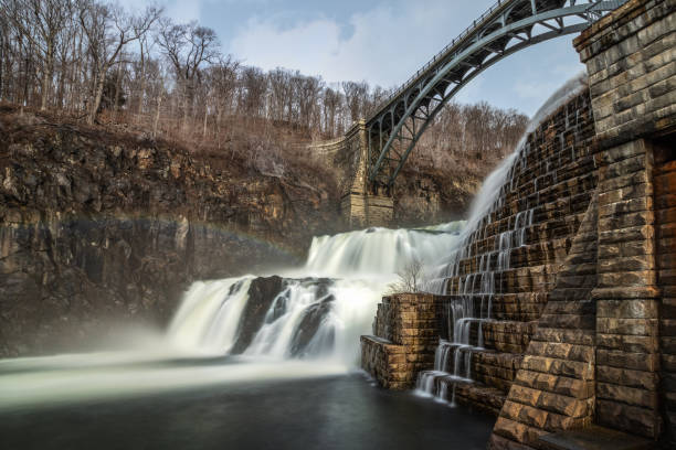 Water cascading down a dam with a bridge arching over the waterfall.