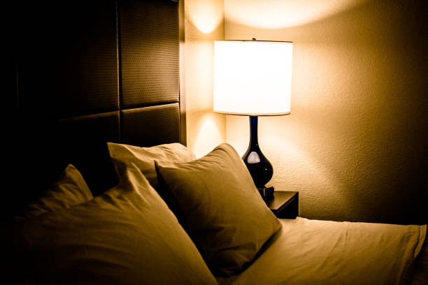 Bedroom at night Illuminated lamp and bed in dimly lit bedroom at night low lighting stock pictures, royalty-free photos & images