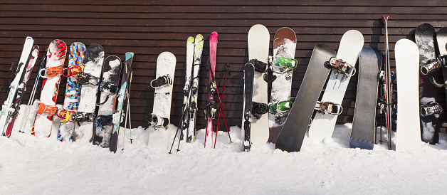 Group of snowboards and skis leaned on wooden wall in ski resort
