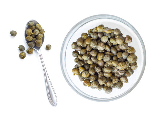 Top view of capers isolated Top view of pickled capers in bowl and spoon. Salted flower buds isolated on white background caper stock pictures, royalty-free photos & images