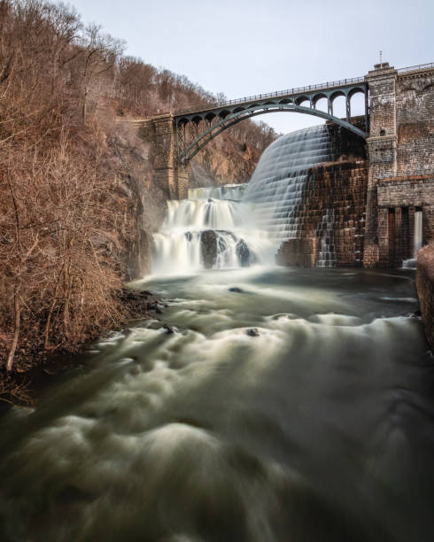 istock Water cascading down a dam with a bridge arching over the waterfall. 1131870213