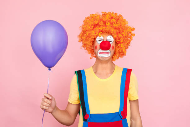 istock Man in a red wig, overalls and makeup cry, holding balloon 1131871443