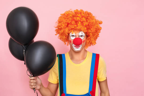 istock Angry man in a red wig, overalls, makeup with black balloon 1131871462