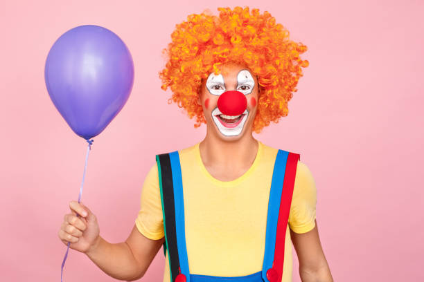 istock Man in a red wig, overalls and makeup holding one balloon 1131871464