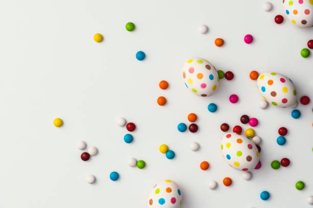 Hand painted colourful spotty easter eggs and colourful chocolate beans on white background. Directly above table top shot.
