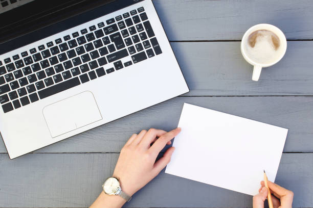 istock Woman hands writing blank paper with laptop and coffee cup. 1131877806