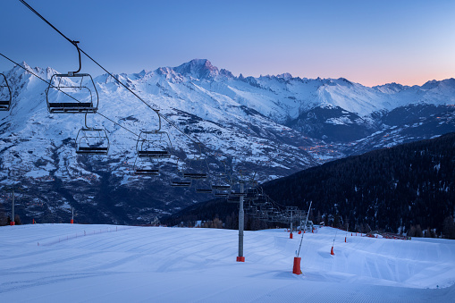 La Plagne ski resort in French Savoy Alps at sunrise in winter. View of snow covered mountains, groomed ski slopes and ski lift. Mountain Mont Blanc in background