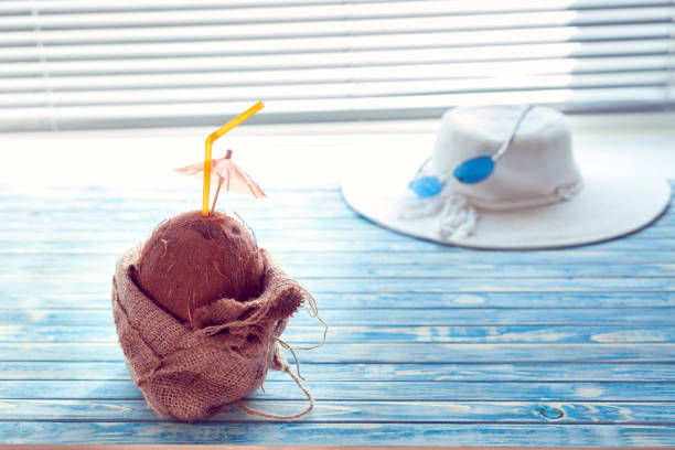 Ready to travel. Coconut with straw is wrapped in burlap on a blue background with white hat and blue sunglasses