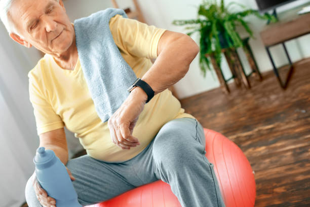 istock Senior man exercise at home sitting on exercise ball checking time 1131883074