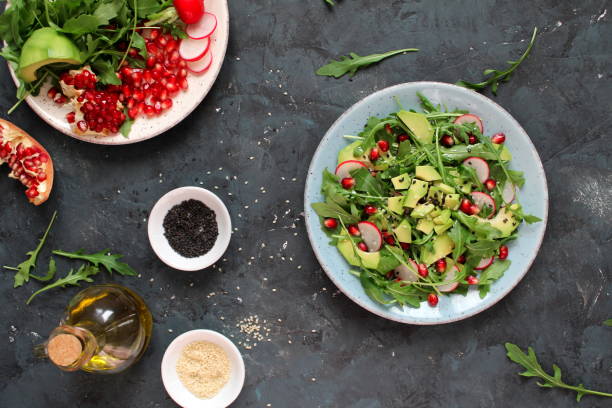 ingedient pour faire la salade sur le fond foncé. salade de légumes en assiette, avocat, roquette, grenade, radis et sésame. - ingedient photos et images de collection