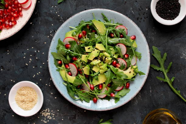 ingedient pour faire la salade sur le fond foncé. salade de légumes en assiette, avocat, roquette, grenade, radis et sésame. - ingedient photos et images de collection