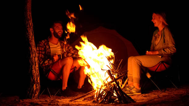 Two campers warming up near campfire, telling funny stories, wild fire risk