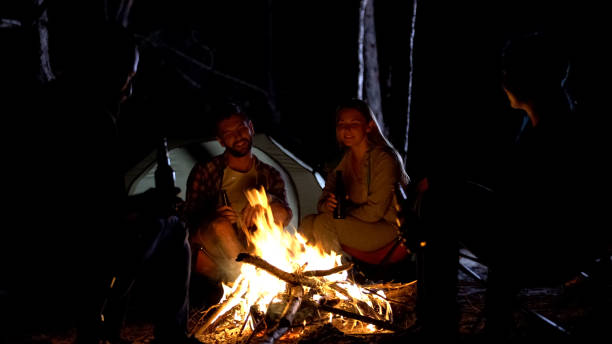 istock Good company sitting around campfire at night, drinking beer and talking, fun 1131888762