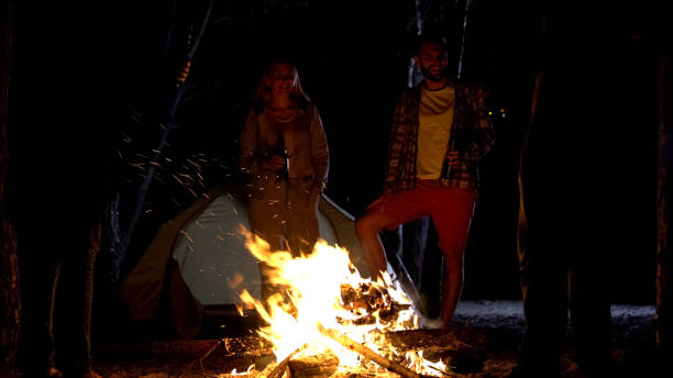 istock Smiling campers standing around bonfire with beer bottles, having great time 1131888799