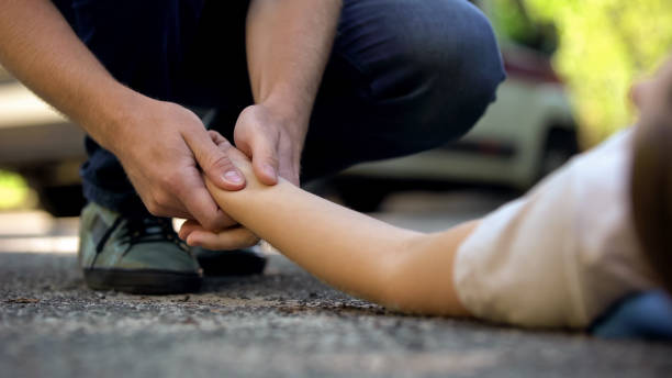 uomo in mano a ragazza sdraiata su strada, vittima incosciente di un incidente stradale, 911 - accident auto accidents car ambulance foto e immagini stock