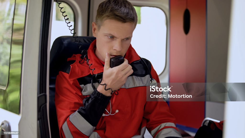 Male paramedic talking by radio, sitting in ambulance, ready to drive on call Dispatcher Stock Photo