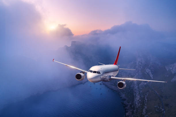 istock Passenger airplane is flying over clouds at sunset. Landscape with white airplane, low clouds, sea coast, purple sky at dusk. Aircraft is landing. Business trip. Commercial plane. Travel. Aerial view 1131890254