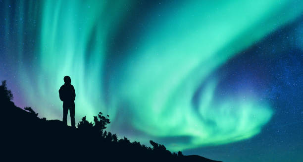 aurora borealis und silhouette einer frau mit rucksack in der nacht. mädchen auf dem hügel, sternenhimmel mit nordlicht. himmel mit sternen und polarlicht. trekking. landschaft mit strahlenden polarlichtern und menschen - raum eine person dunkelheit stehen gegenlicht stock-fotos und bilder